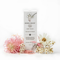 Bondi Wash Baby Balm box standing upright on a white background, styled with pink and white flowers in front. The box is white with black text and floral line art, and the product name reads Baby Balm with Blue Cypress & Petitgrain.