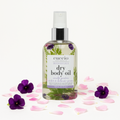 Bottle of Cuccio Naturals dry body oil with violet and delicate peony flowers on a white background