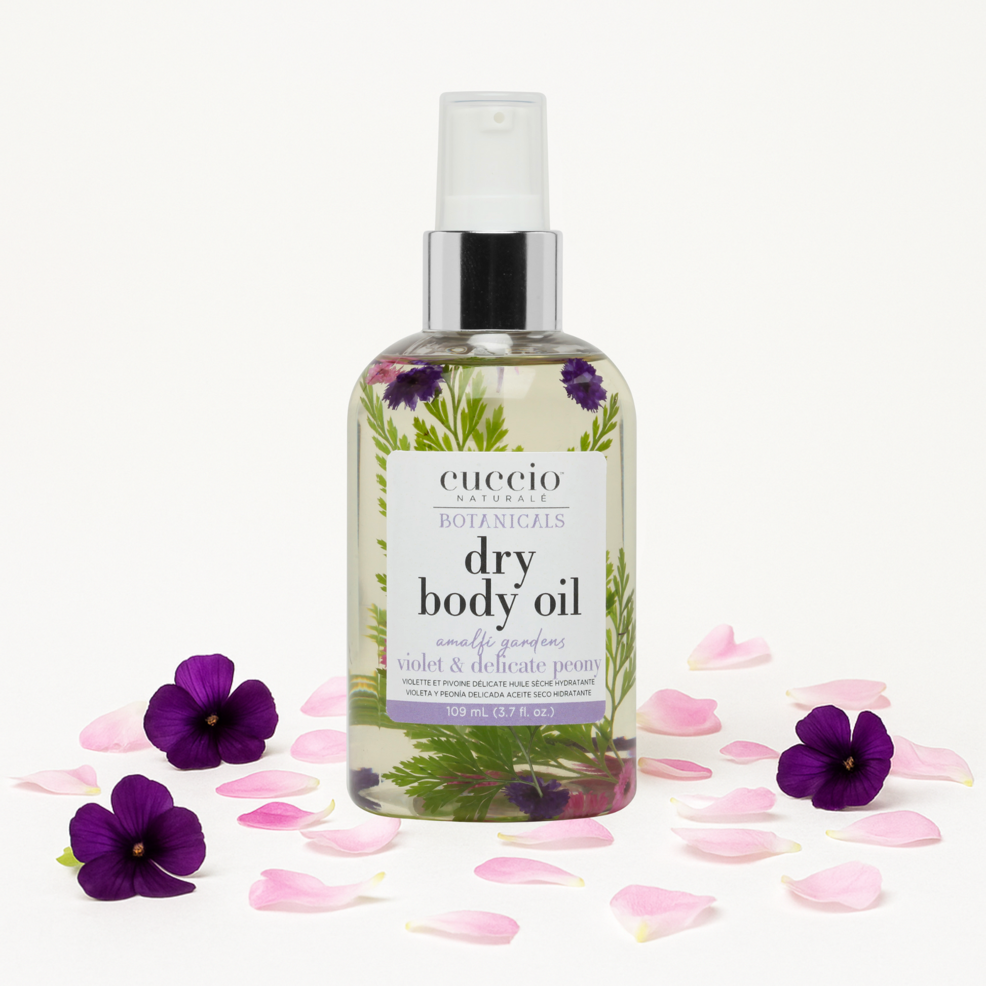 Bottle of Cuccio Naturals dry body oil with violet and delicate peony flowers on a white background