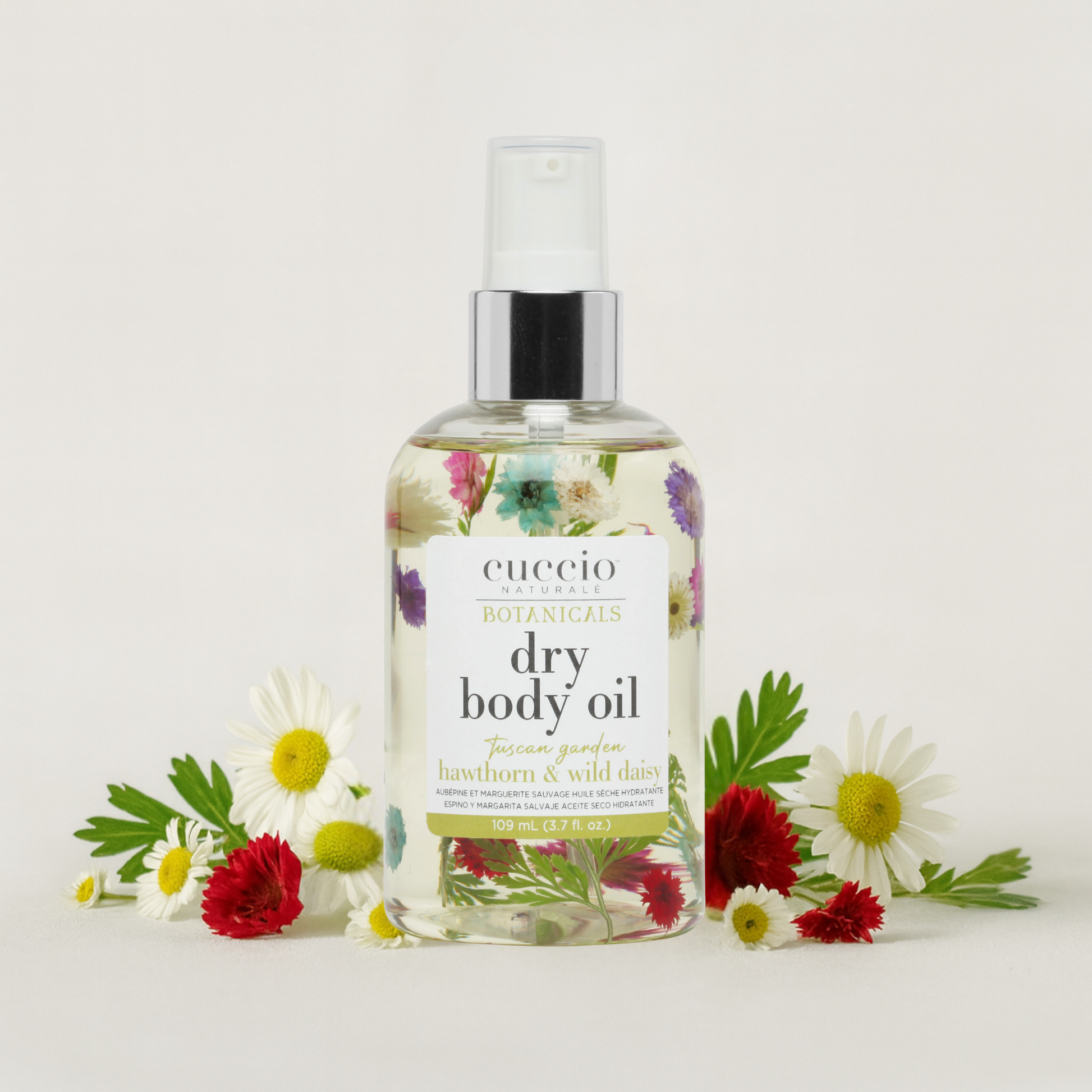 Cuccio Botanicals dry body oil bottle with hawthorn and wild daisy flowers on a light background