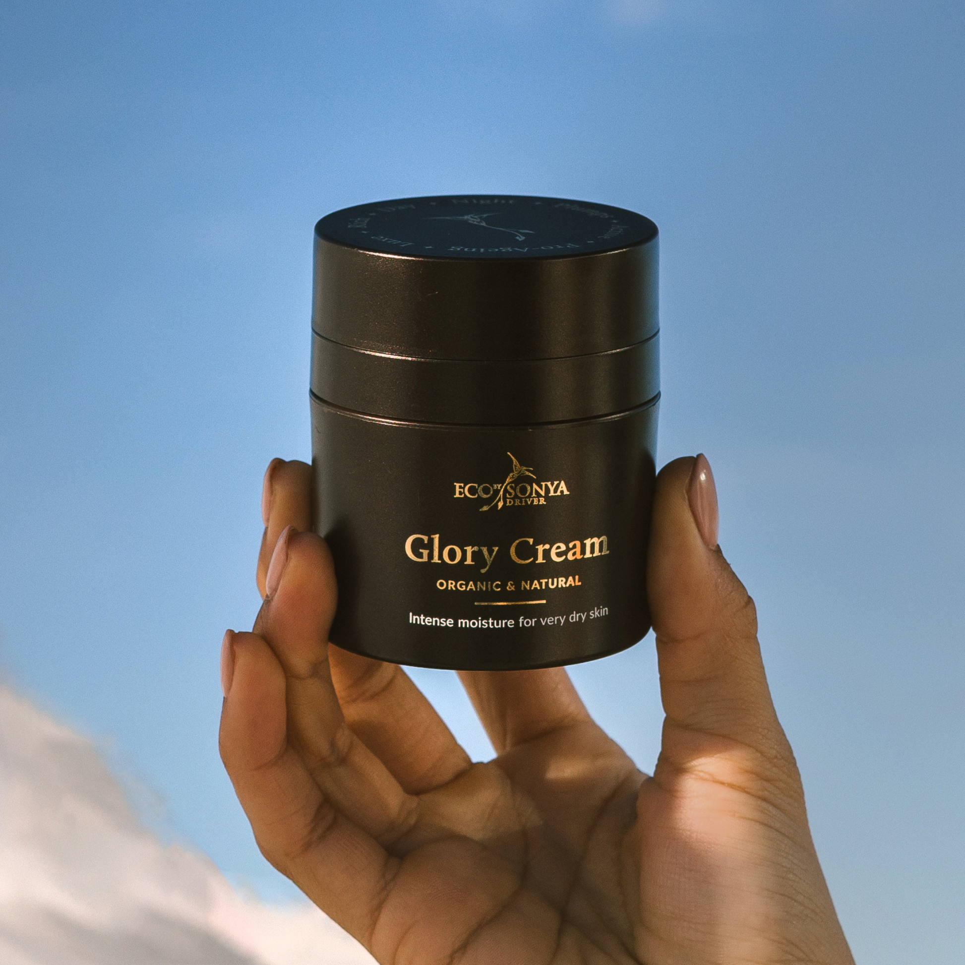 Hand holding a jar of Eco by Sonya Glory Cream against a clear blue sky