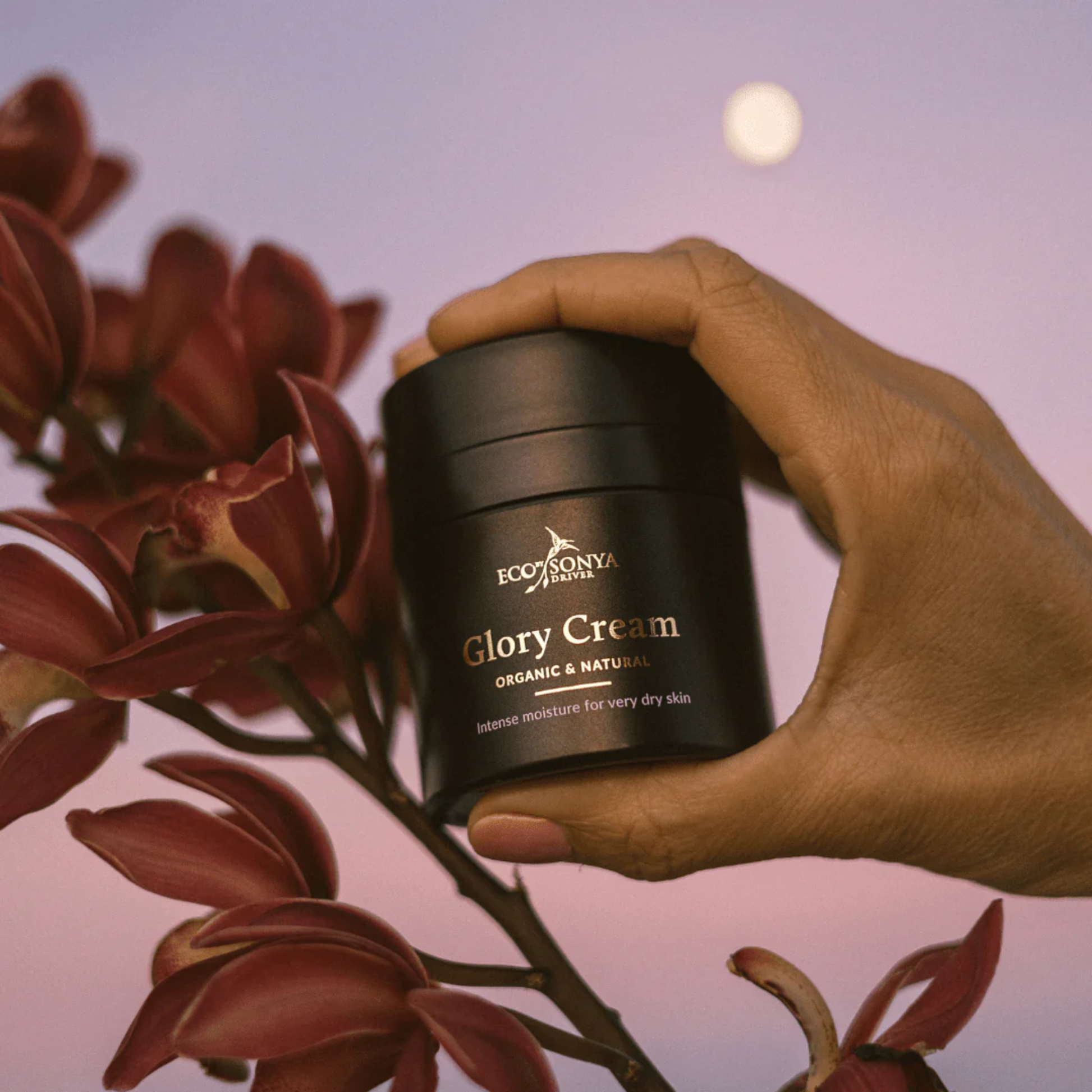 Hand holding a jar of Eco Tan Sonya Glory Cream with flowers and moon in the background