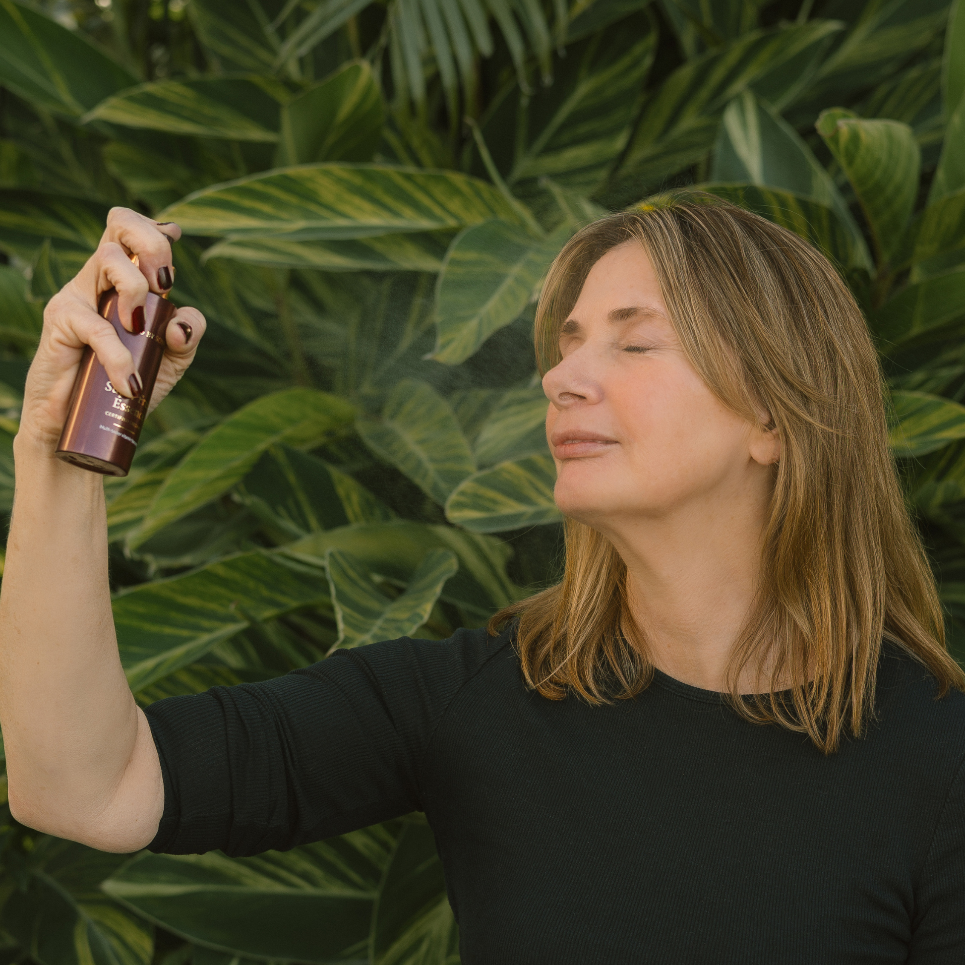 Woman holding a Super Fruit Essence bottle against a green leafy background