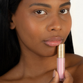A close-up of a woman holding a pink lip gloss tube Eco by Sonya Glory Gloss Candy 21 with a gold cap against a clean white background.