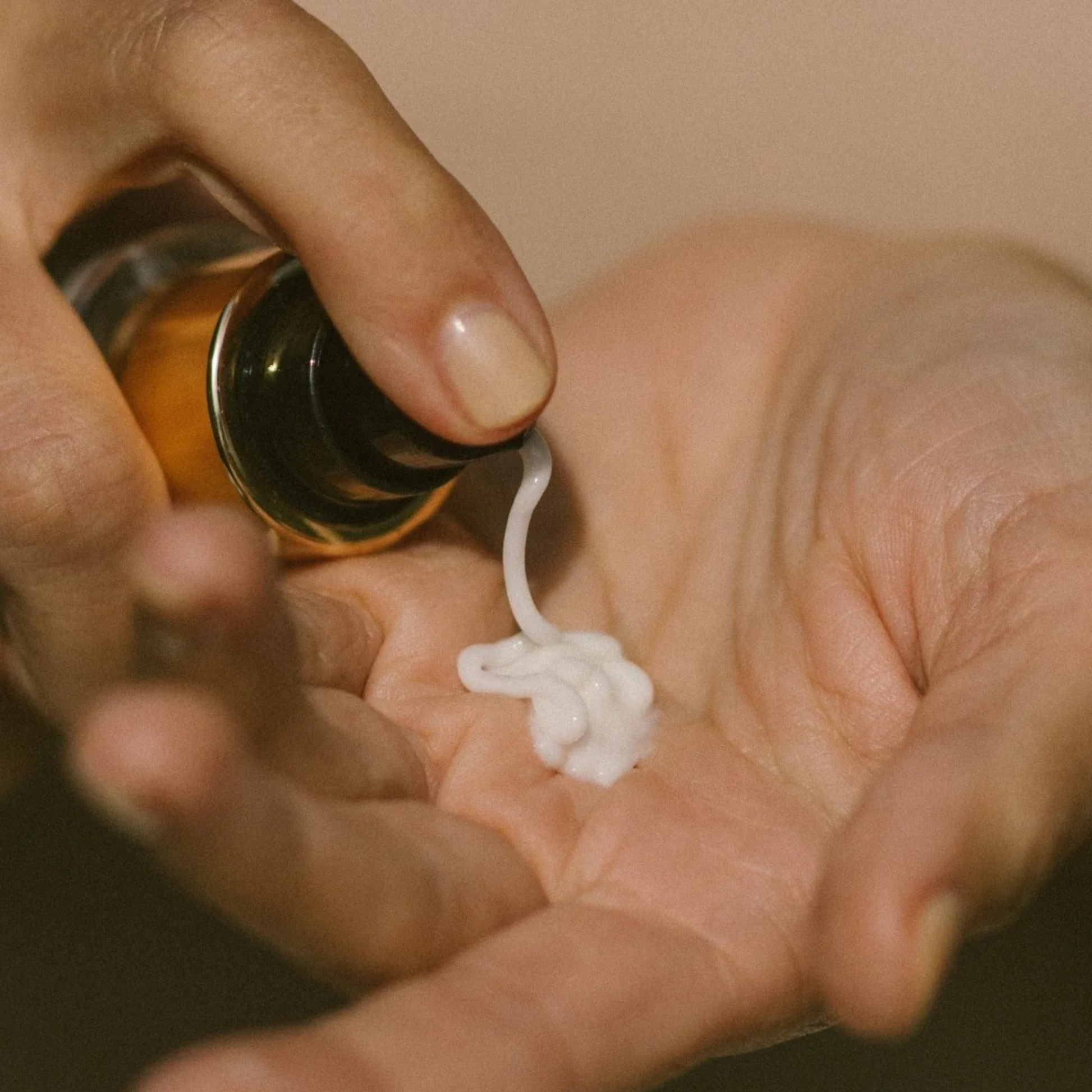 Hand holding a bottle of skincare product with a small amount of white Super Fruit Hydrator cream on an open palm