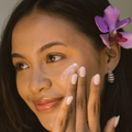Woman applying Super Fruit Hydrator cream to her face with a purple flower in her hair
