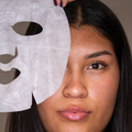 Woman holding a white sheet mask over her face