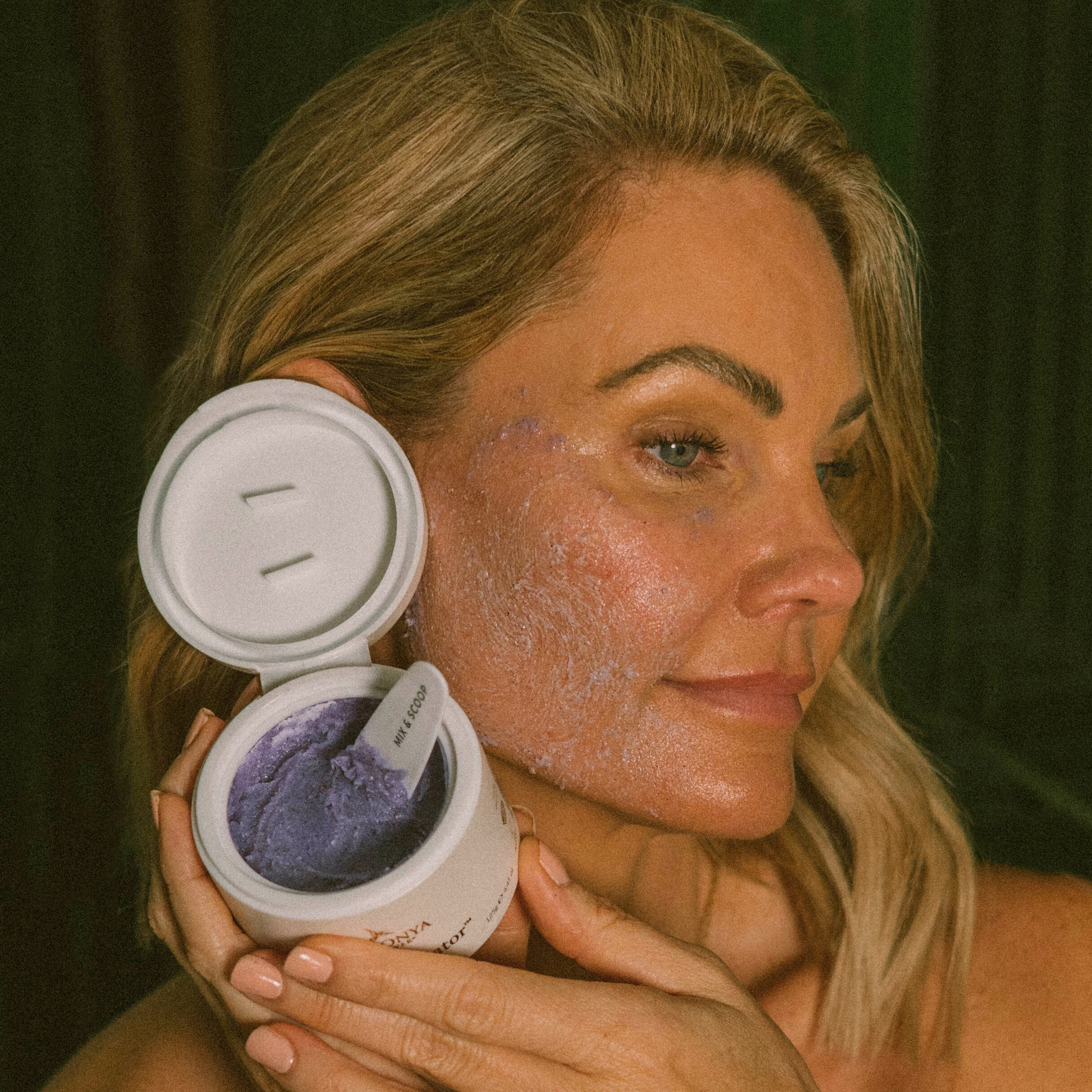 Woman applying Eco by Sonya Super Acai exfoliator  to her face with  a container of the scrub.
