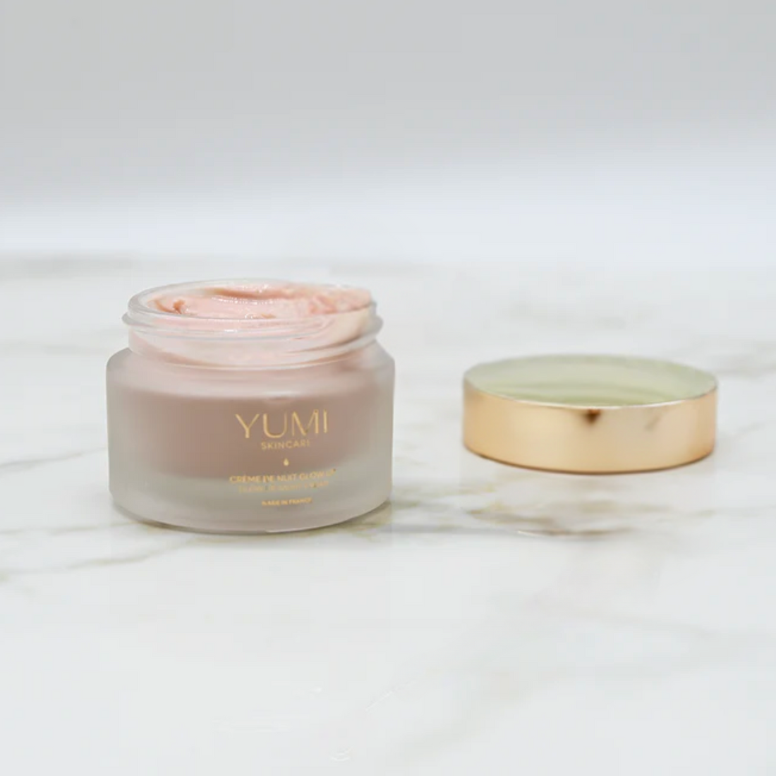 YUMI skincare cream jar with gold lid on a white background
