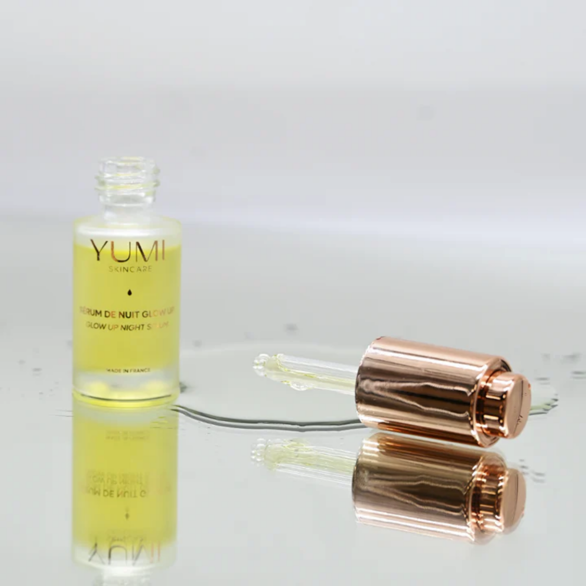 YUMI skincare serum bottle with rose gold cap on a reflective surface