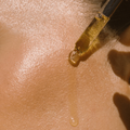 Close-up of a dropper with a yellow liquid on a beige skin-like surface