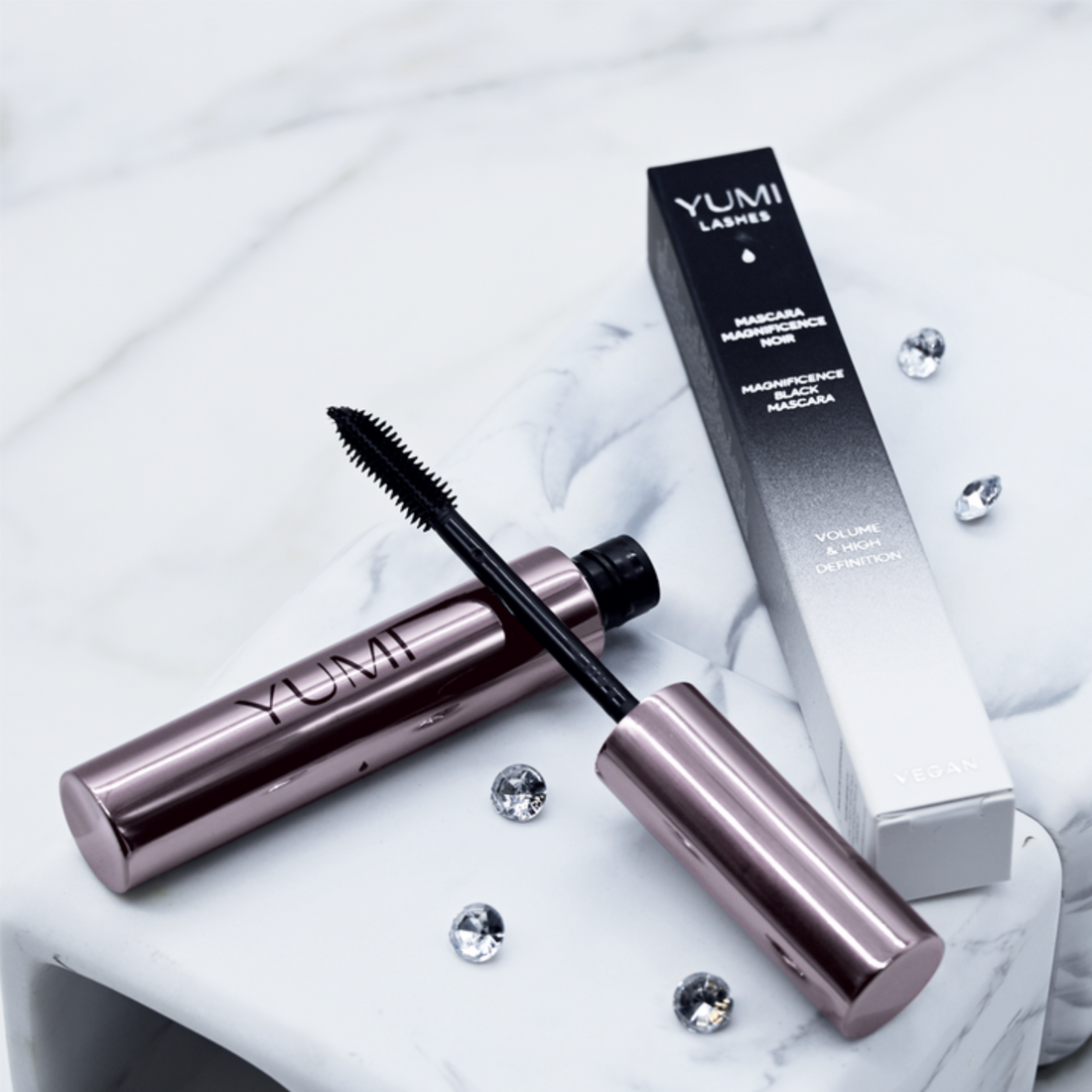 Display of Yumi Beauty Yumi Lashes Magnificence Black Mascara with multiple mascara tubes on a clear stand.